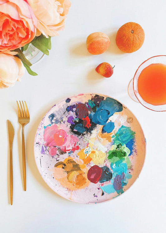 paint palette with paint on white ceramic plate beside silver fork and knife