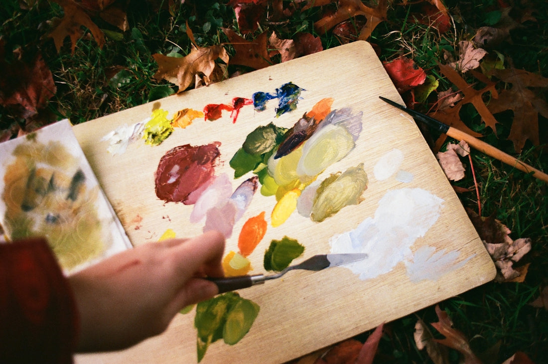 Artist mixes paints on a wooden palette outdoors.