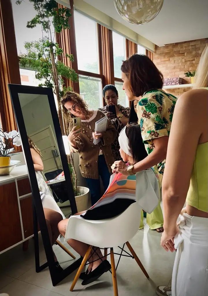 Students practicing draping on a client in front of a mirror during a Drops de Cor training